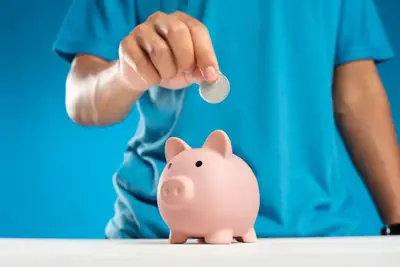 Hand dropping a coin into a pink piggy bank