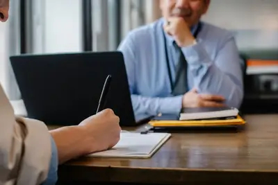 Job candidate filling out paperwork across a desk from an interviewer with a laptop