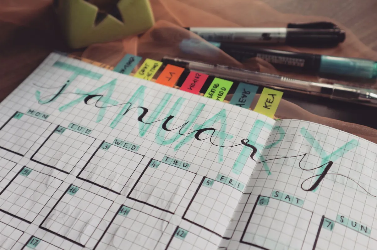 Hand-lettered monthly planner page with colored tabs and pens