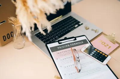 Clipboard with a pricing formula next to a laptop