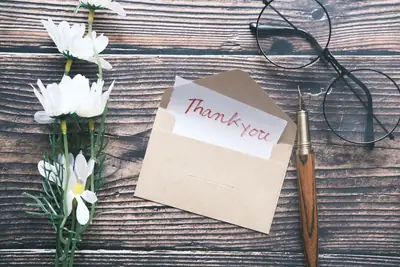 Handwritten thank-you note in a kraft envelope next to a pen and glasses