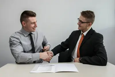 Two professionals shaking hands across a table after agreeing on a job offer