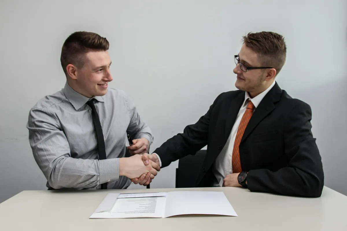 Two professionals shaking hands across a table after agreeing on a job offer