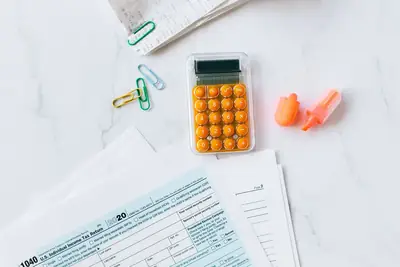 IRS tax forms, a calculator, and paper clips on a white desk
